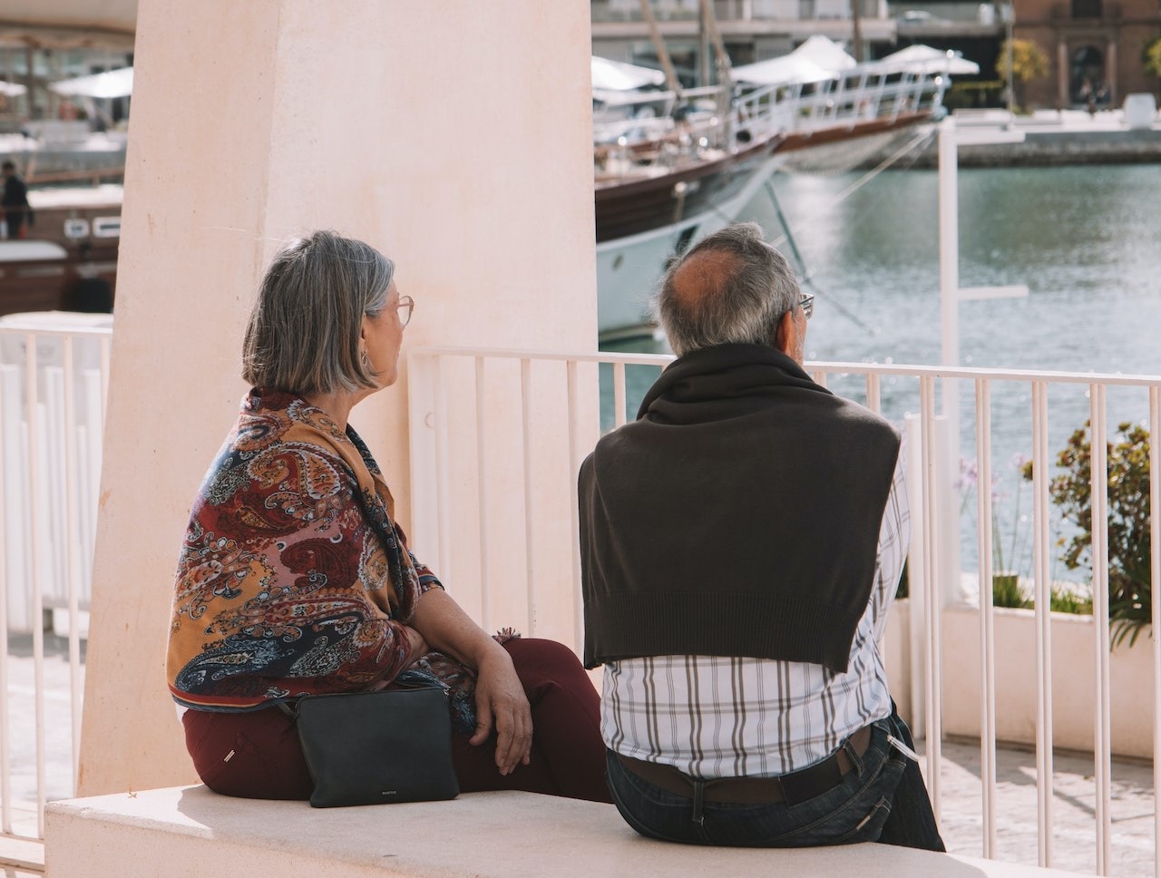 A person and person sitting on a bench looking at boatsDescription automatically generated